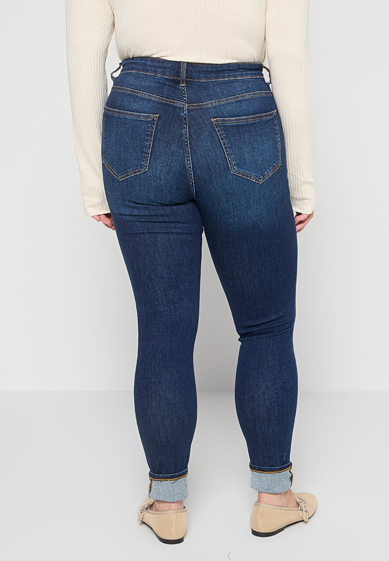 Dunkelblaue, figurbetonte Jeans mit hoher Taille. Merkmale beinhalten Gesäßtaschen, umgeschlagene Säume und Kontrastnähte. Aus Denim-Stoff gefertigt.