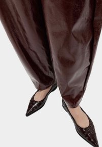 Brązowe szerokie spodnie z ekoskóry w połączeniu z czarnymi balerinami o spiczastych noskach, zdobionymi metalowymi oczkami i gładką fakturą.