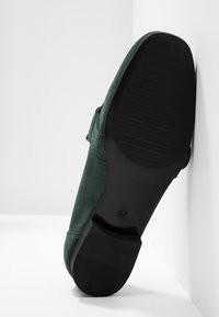 Chaussure en suède vert avec une semelle en caoutchouc noir. Le talon est bas et la semelle présente des rainures horizontales pour une meilleure traction. Taille indiquée : 37.