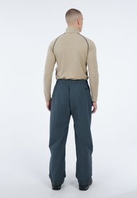 Beige lange mouw top met hoge kraag en donkere stiksels, gecombineerd met losse donkerblauwe broeken, voorzien van elastische tailleband en verstelbare manchetten.