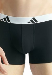 Czarne bokserki z białym paskiem w talii z trzema czarnymi paskami. Wykonane z gładkiego materiału, podkreślające dopasowany krój i minimalne szwy.