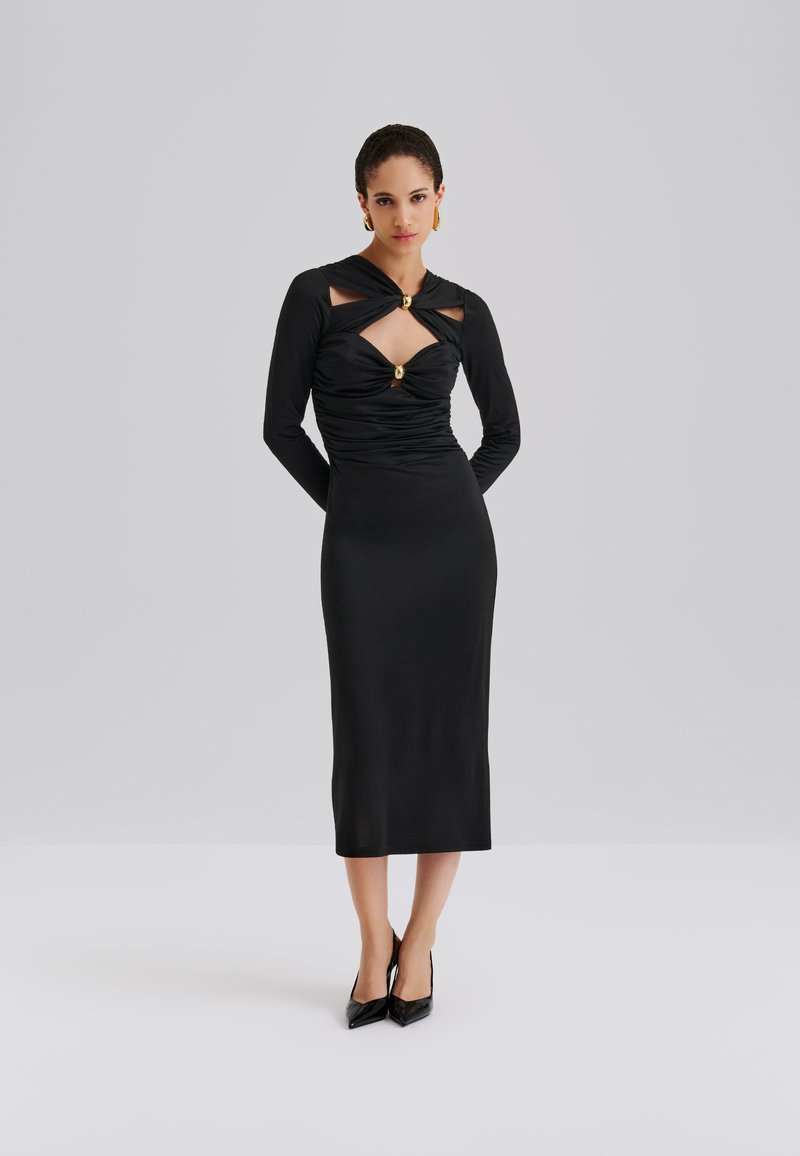 Must pikkade varrukatega kleit, millel on lõigatud detailid ja kuldne aktsent, vormiv siluett ja sile tekstuur, ulatudes keskpikani vasikas.