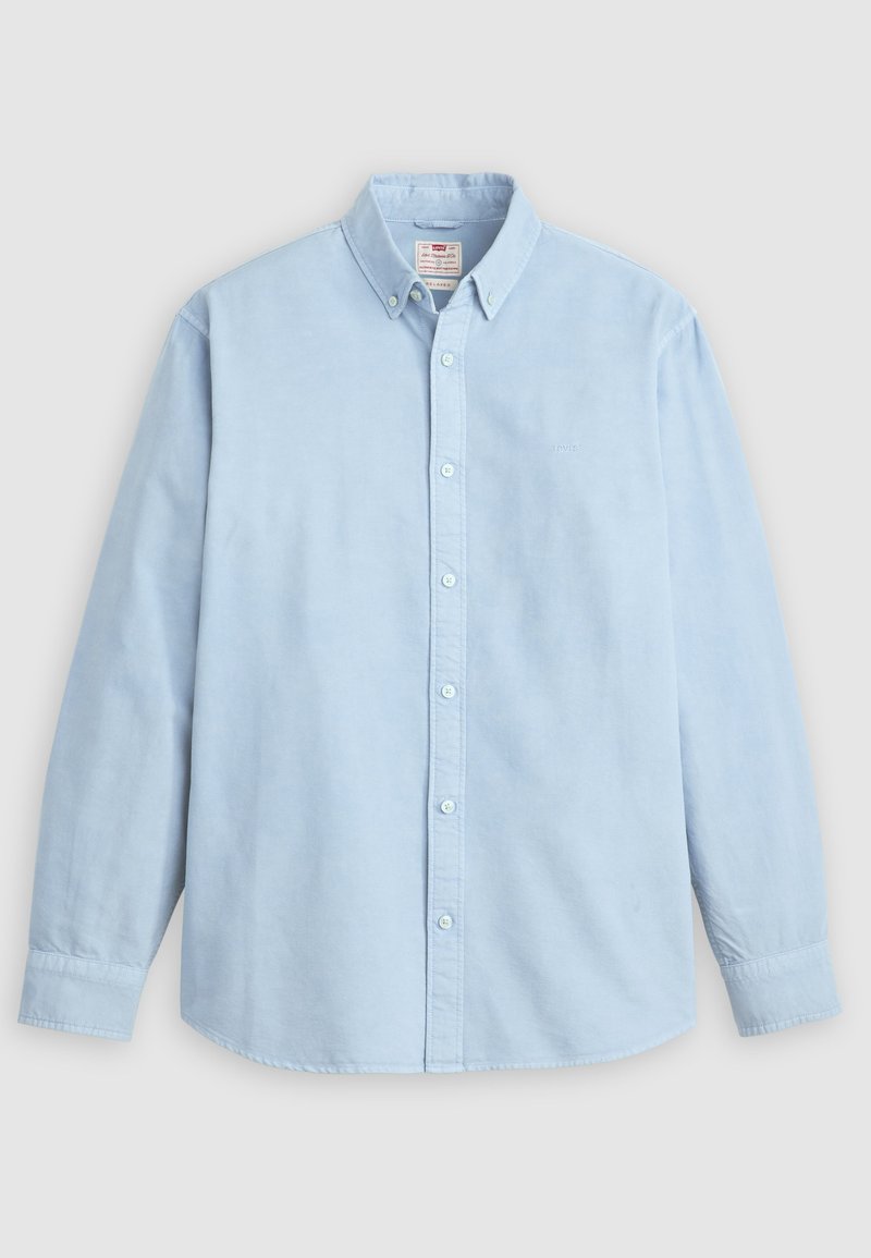 Camisa de manga larga azul claro con botones, cuello abotonado y un único bolsillo en el pecho, colocada sobre un fondo gris.