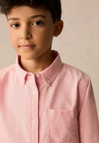 Camicia button-up rosa chiaro in cotone con colletto, tasca anteriore e logo ricamato nell'area della tasca.