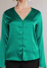 Vihreä satiinipaita pitkillä hihoilla, v-pääkohdalla ja sileällä pinnalla. Sisältää hienovaraiset sauman yksityiskohdat ja rento istuvuus.