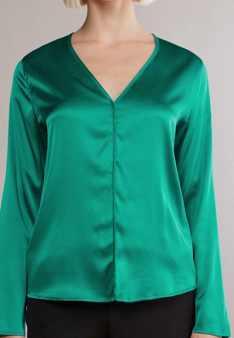 Vihreä satiinipaita pitkillä hihoilla, v-pääkohdalla ja sileällä pinnalla. Sisältää hienovaraiset sauman yksityiskohdat ja rento istuvuus.