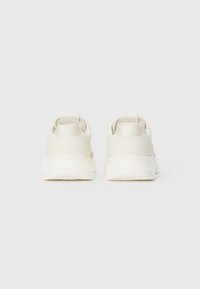 Baskets beige clair avec une tige synthétique lisse, un col rembourré et une semelle en caoutchouc épaisse. Présente un design minimaliste sans marque visible.