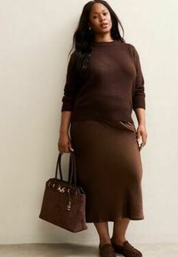 Bruine gebreide trui en een aansluitende rok met een gladde textuur. Gecombineerd met een donkerbruine handtas en bijpassende loafers.
