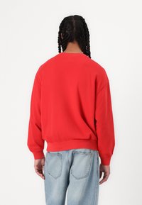 Sudadera roja de cuello redondo con hombros caídos y puños acanalados, acompañada de jeans de corte relajado en un tono azul claro. Textura de tejido suave.