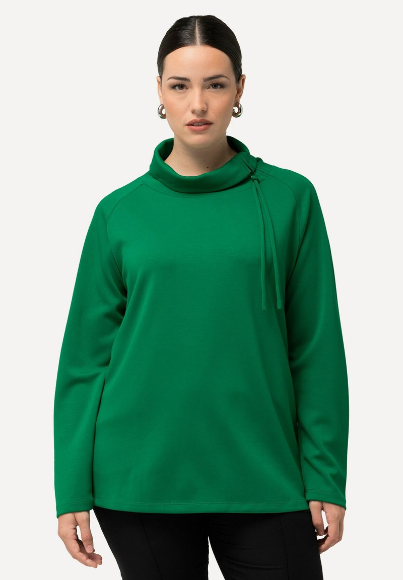 Felpa verde con colletto alto, maniche lunghe e vestibilità rilassata. Presenta un dettaglio decorativo con nodo sulla spalla sinistra. Texture morbida.