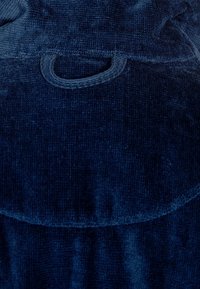 Dunkelblaues Cordstoff mit weicher Textur, ausgestattet mit einer Gesäßtasche und einem abgerundeten Klappen-Detail am oberen Rand.