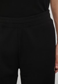 Svarta sweatpants med en slät textur, elastisk midja och ton-i-ton sömmar. Har en subtil logotyp i guld på låret.