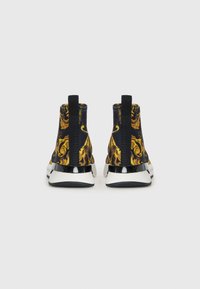 Sneakers alla caviglia neri e oro con un audace motivo floreale, tomaia elastica e dettagli lucidi neri sul tallone, completati da una suola bianca.