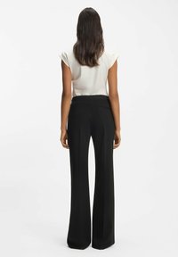 Sorte vidde bukser med glat tekstur, der har høj talje og baglomme, kombineret med en lysefarvet top med korte ærmer.