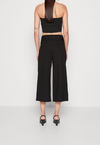 Svarta vida byxor i slätt tyg, med hög midja, knappstängning och en kortad design ovanför ankeln.