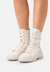 Botas altas blancas de cuero con diseño de cordones, cremallera lateral y suela de goma texturizada con estrías pronunciadas.