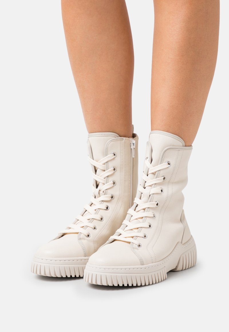 Botas altas blancas de cuero con diseño de cordones, cremallera lateral y suela de goma texturizada con estrías pronunciadas.