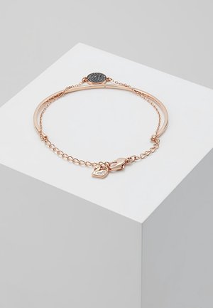 Roze gouden armband met ketting en zwarte ovale bedel, met een kleine hartvormige bedel met ingelegde kristallen op een witte displayblok.
