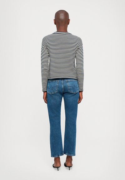 Gestreiftes schwarz-weißes Langarmoberteil, kombiniert mit blauen, geraden Jeans mit Gesäßtaschen und entspannter Passform, getragen mit schwarzen Absätzen.