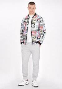 Bomber jacket with colorful comic-style prints, black accents; paired with gray sweatpants and white sneakers. Plain white t-shirt underneath.