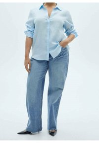 Chemise bleu clair à manches longues avec col, associée à un jean en denim clair à taille haute et ample, et des chaussures noires à bout pointu.