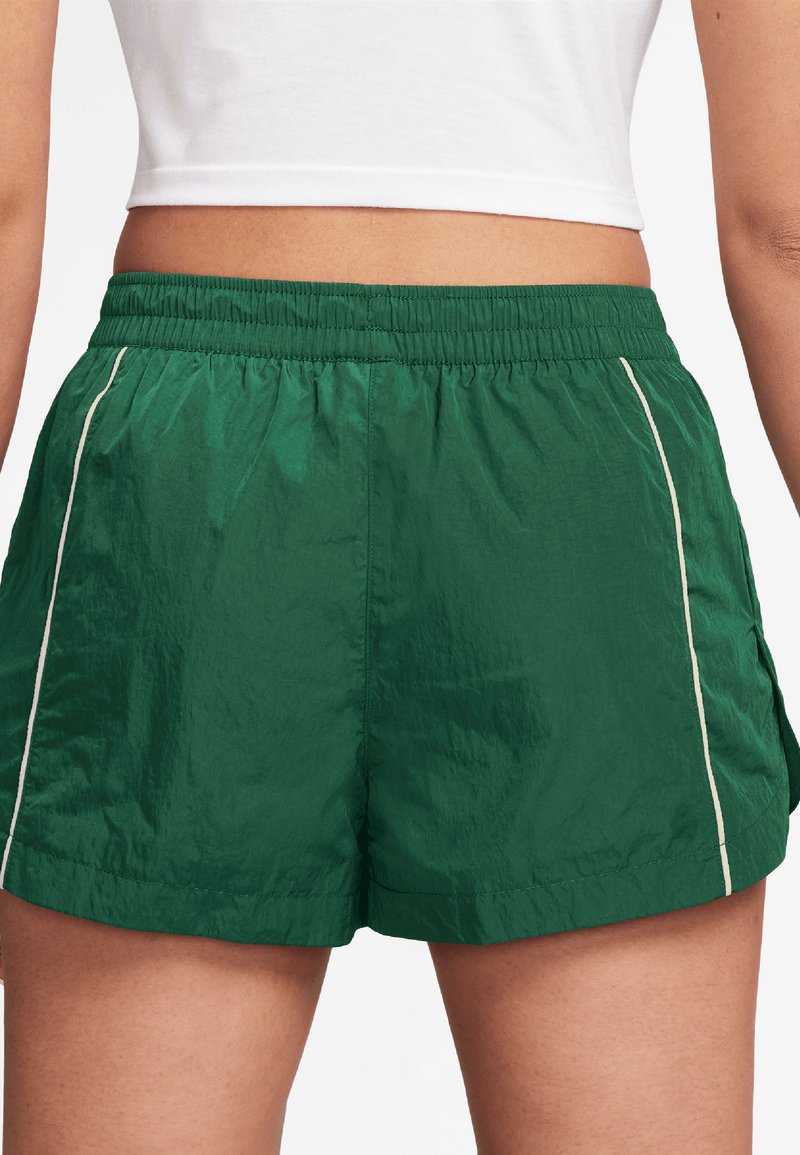 Shorts verts, légers, avec taille élastique, dotés de poches latérales et d'un passepoil blanc le long des coutures. Matière texturée, résistante à l'eau.
