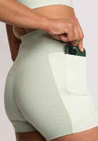 Pantaloni sportivi verde chiaro con tasca laterale per il telefono, realizzati in tessuto liscio ed elasticizzato, dotati di un alto punto vita e design senza cuciture.