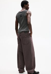 Top grigio senza maniche e pantaloni larghi viola scuro con cuciture visibili, tasche posteriori e un'etichetta in pelle nera sulla cintura.