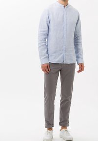 Camicia a maniche lunghe in lino azzurro chiaro con colletto alla mandarino, caratterizzata da una chiusura con bottoni davanti e abbinata a pantaloni grigi e sneaker bianche.