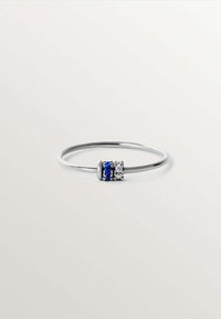 Anillo de plata esterlina con una banda delgada, que presenta un embellecimiento central de piedras preciosas azules y claras en un diseño circular.
