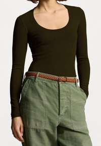 Bodysuit de manga larga acanalado en verde oliva con un escote ancho, combinado con pantalones cargo verdes holgados y un cinturón trenzado marrón.