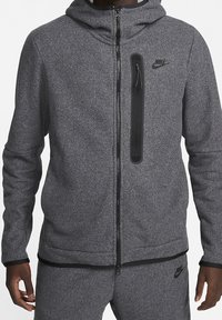 Gray zip-up hoodie made from textured fabric with a front zip pocket and black accents. Features a hood and ribbed cuffs. Nike logo visible.