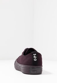 Lila kanvas sneakers med låg profil och texturerad ovandel, med en svart hälflik med vit branding och gummisula.