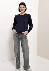 Felpa blu navy con maniche lunghe e strisce laterali, abbinata a jeans a gamba larga grigio chiaro e sneakers bianche. Design semplice e casual.