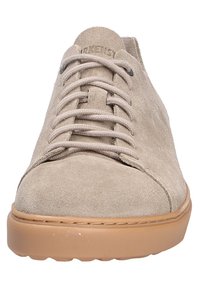 Chaussure en suède beige avec bout rond, lacets à l'avant et semelle en caoutchouc marron clair. Texture lisse et design minimaliste.