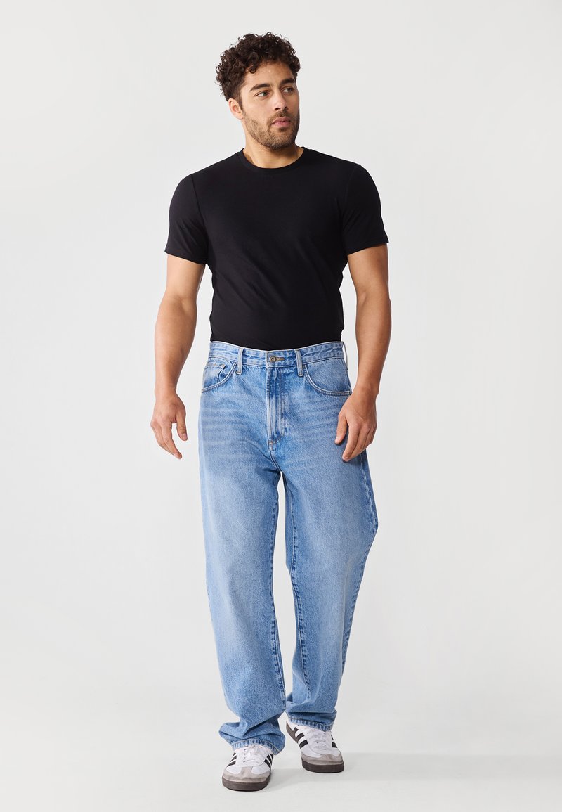 Herrenoutfit mit einem schwarzen Kurzarm-T-Shirt und hellblauen, locker sitzenden Jeans mit normalem Bund und dezenten Used-Details.
