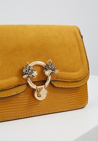 Borsa in suede giallo con dettagli in tessuto a croco, caratterizzata da una chiusura metallica dorata con accenti a forma di testa di leopardo e bordi cuciti.