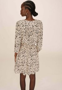 Robe à manches courtes avec un motif abstrait crème et noir. Elle présente un dos froncé, une taille élastique et un tissu texturé.