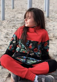 Kolorowy zestaw sportowy składający się z czerwonej bluzki z wysokim kołnierzem, kwiatowym wzorem oraz czarnych spodni z czerwonymi akcentami. Miękka tkanina, luźny krój.