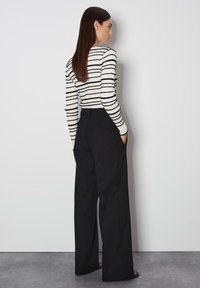 Pantalons larges noirs associés à un pull rayé noir et blanc, avec une silhouette ajustée et des manches longues. Texture de tissu lisse.