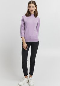 Un pull en tricot côtelé de couleur lilas clair avec un col montant et des manches trois-quarts, associé à un jean skinny noir et des baskets blanches.