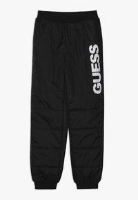 Černé prošívané teplákové kalhoty s elastickým pasem, bočními kapsami a výrazným bílým logem "GUESS" tištěným na levé noze. Texturovaná látka.