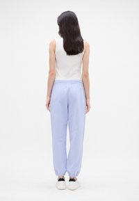 Heledad sinine dressipüksid elastse vöökoha ja otsadega, koos valge ilma varrukateta topiga, nähtuna tagant. Sile tekstuur.