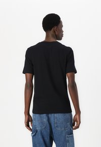 Black cotton t-shirt with short sleeves and a crew neckline, viewed from the back, paired with blue denim pants.