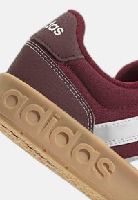 Talon de basket Adidas marron avec des rayures blanches, des coutures blanches et une semelle en caoutchouc épaisse de couleur beige embossée du logo Adidas.