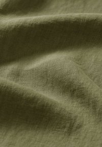 Tessuto di lino in verde oliva, texture con fibre naturali, che mostra leggere pieghe e grinze per un aspetto morbido e flessibile.