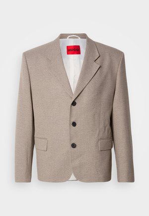 Beige op maat gemaakte blazer met gestructureerde schouders, een enkelgesloten ontwerp, drie zwarte knopen, twee voorzakken en HUGO-label in het rood.