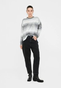 Svetlosivý a tmavosivý pruhovaný sveter s voľným strihom a okrúhlym výstrihom, kombinovaný s čiernymi džínsami s vysokým pásom a čiernymi členkovými čižmami.