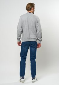 Grå hettegenser med rund hals, strikkede mansjetter og hem. Par med blå denimjeans med rett passform. Hvite sneakers med blå detaljer.