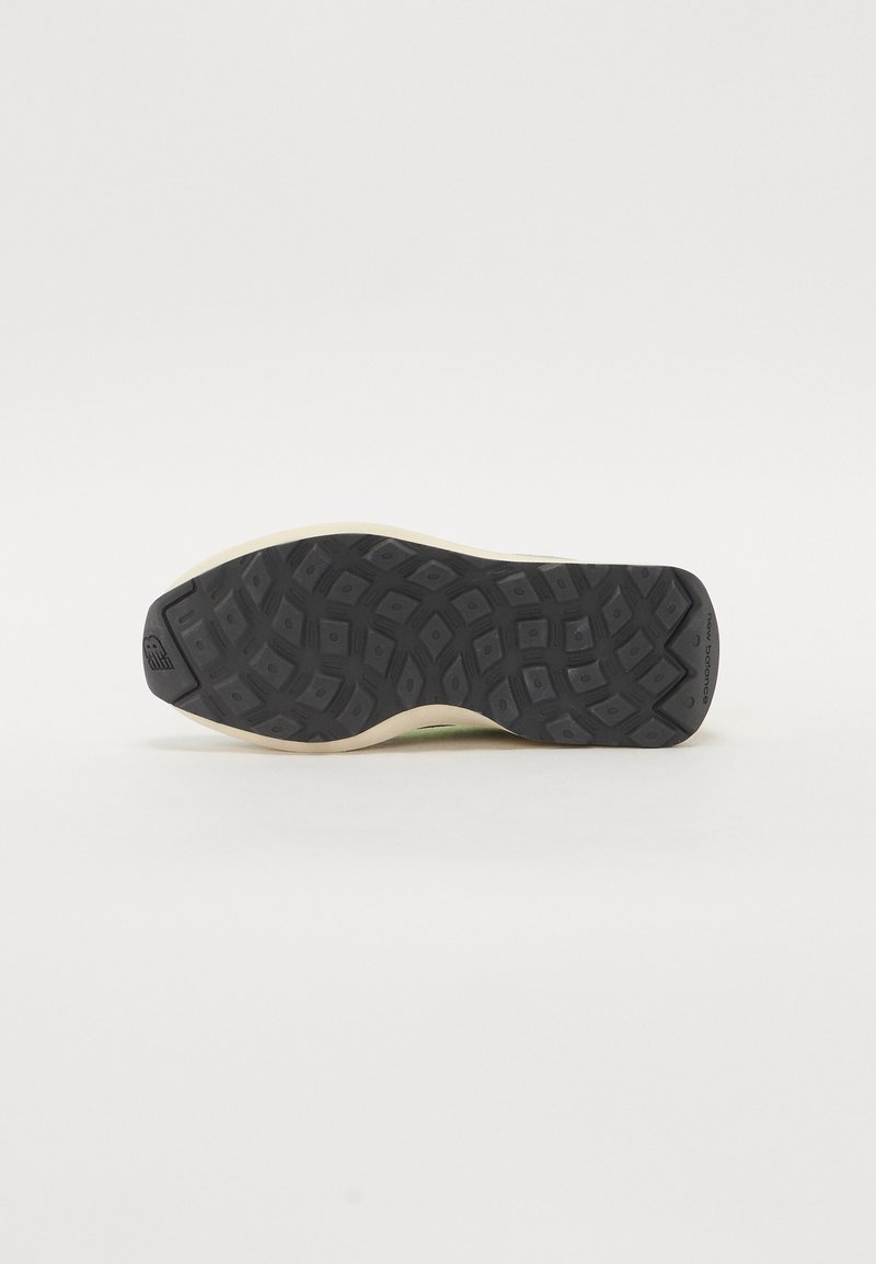 Schwarze Gummisohle eines Sneakers mit strukturiertem Profil, ausgestattet mit einem beigen seitlichen Akzent und Branding an der Ferse.